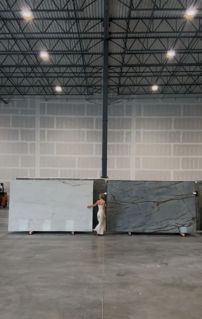 Wide view of a warehouse with large stone slabs on display, showing a person examining the materials.