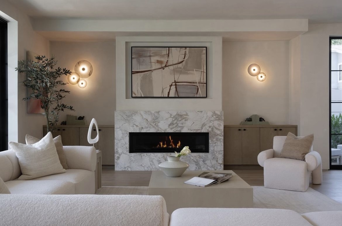 An elegant, contemporary living room with a neutral palette. The fireplace surround is made of light grey and white marble, specifically Invisible Blue Azerocare Leathered marble