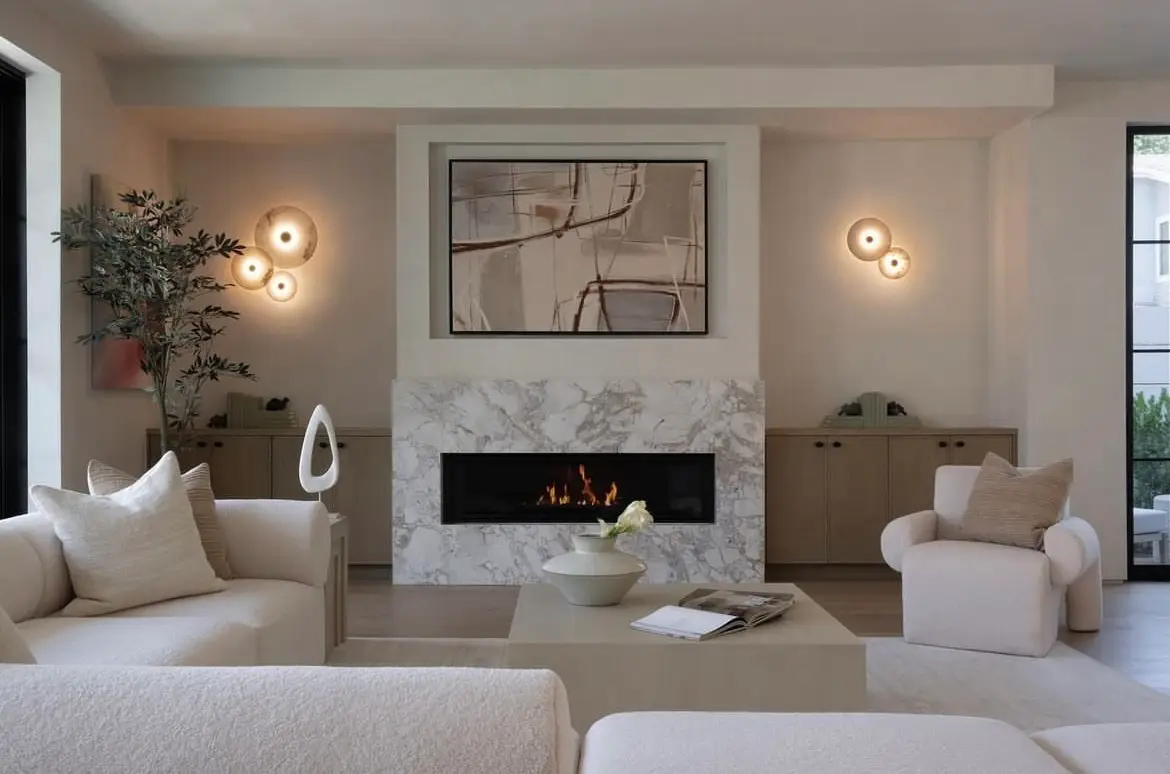 An elegant, contemporary living room with a neutral palette. The fireplace surround is made of light grey and white marble, specifically Invisible Blue Azerocare Leathered marble