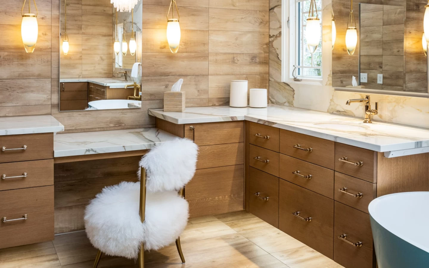 A luxurious bathroom vanity area featuring light wood-look tile on the walls and floor. The countertops are Calacatta Imperiale Porcelain, with golden-brown veining, complementing the wood cabinetry and brass hardware.