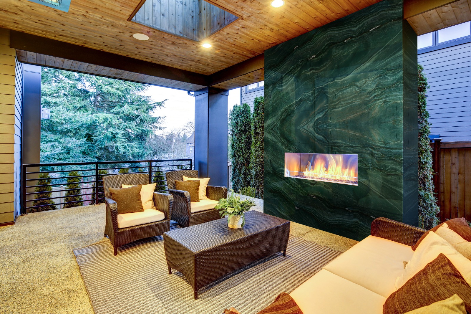 A luxurious outdoor covered patio featuring a vertical fireplace wall clad in stunning, dark green Persa Green Quartzite with high-contrast black veining
