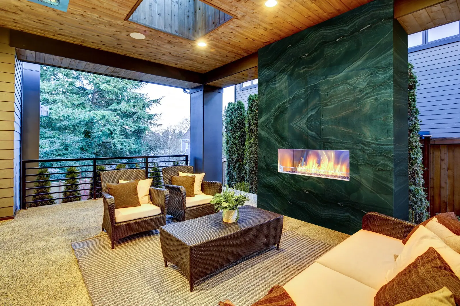 A luxurious outdoor covered patio featuring a vertical fireplace wall clad in stunning, dark green Persa Green Quartzite with high-contrast black veining