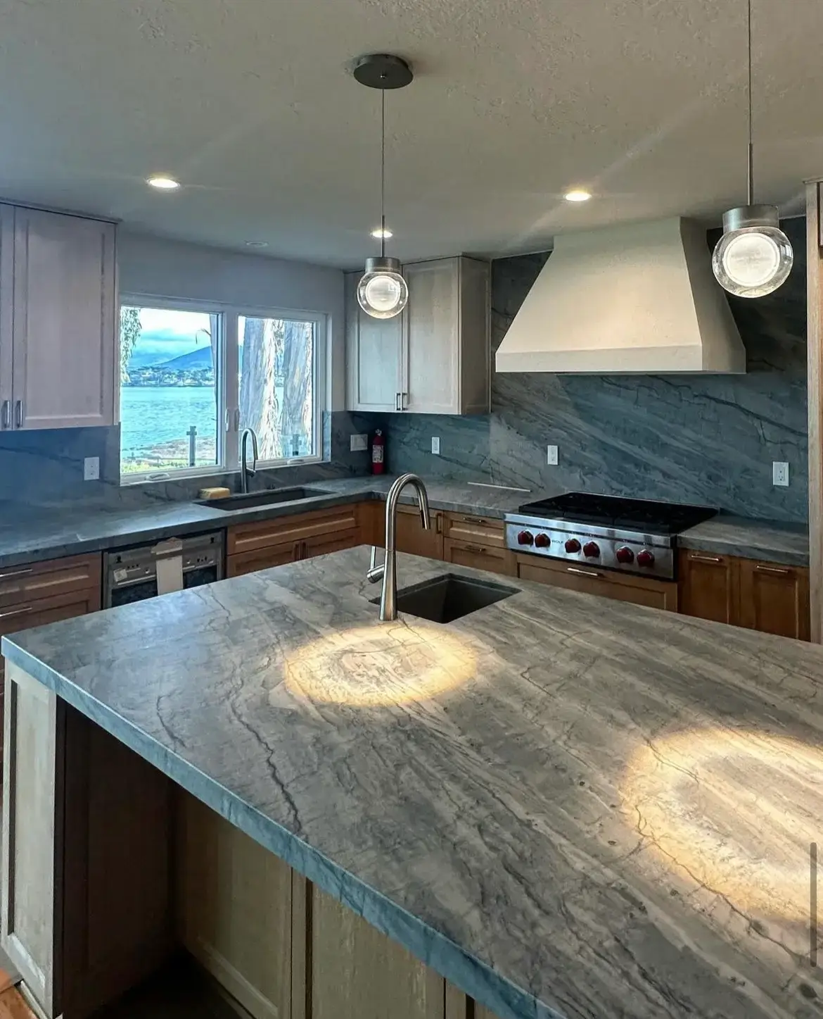 Coastal kitchen with blue-gray quartzite countertops, matching full-height backsplash and ocean view