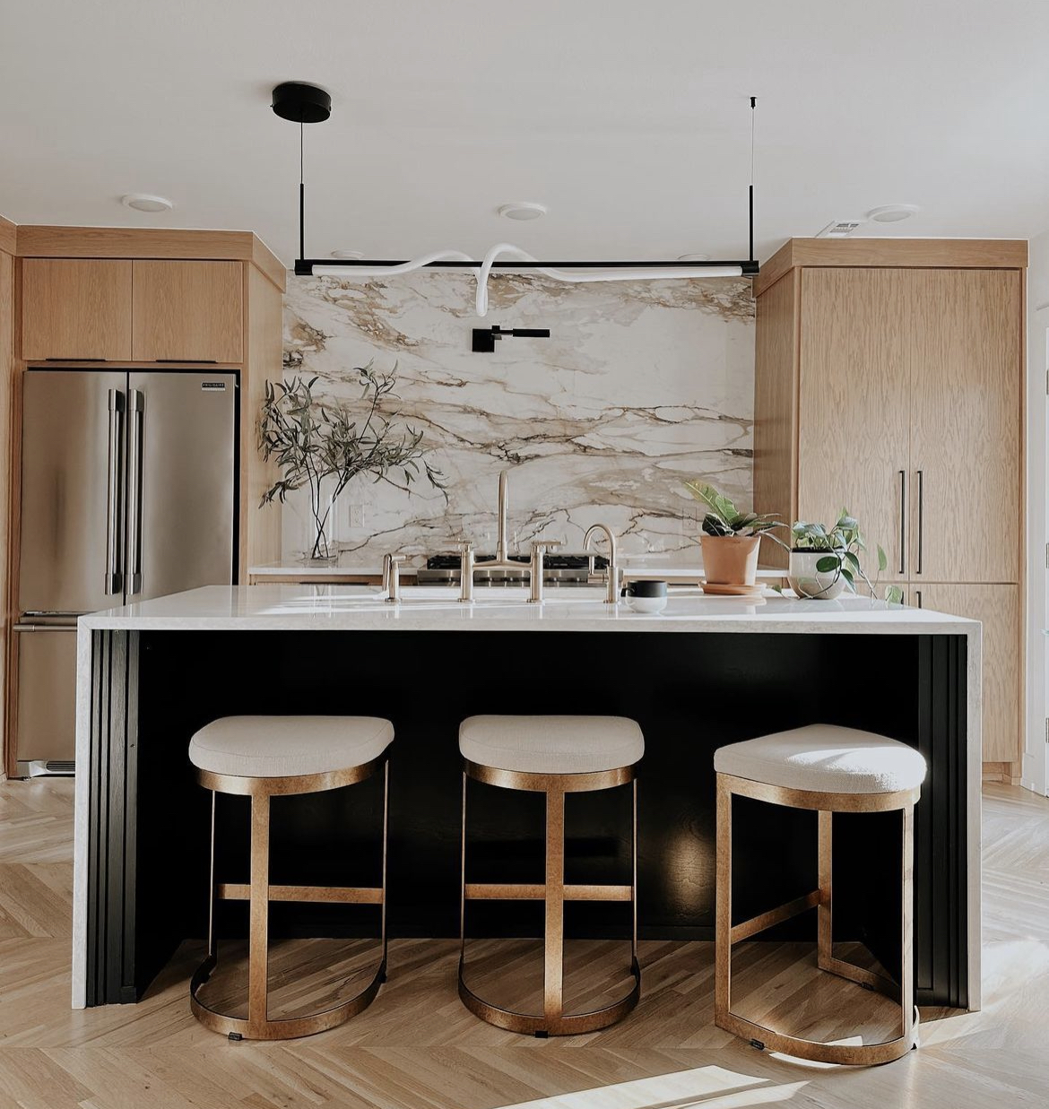 Modern kitchen with Calacatta marble backsplash, black island base, oak cabinetry and brass bar stools