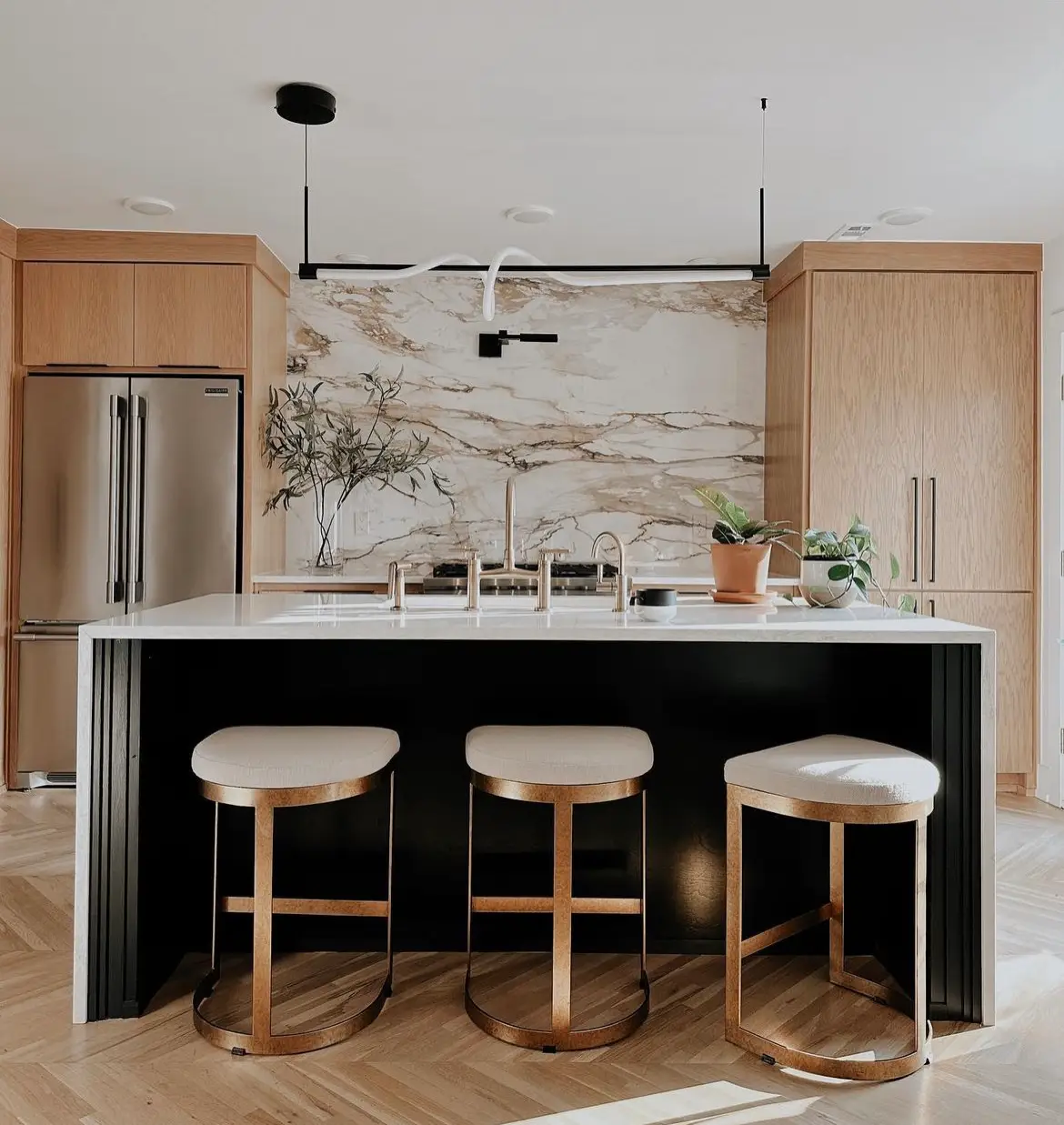 Modern kitchen with Calacatta marble backsplash, black island base, oak cabinetry and brass bar stools