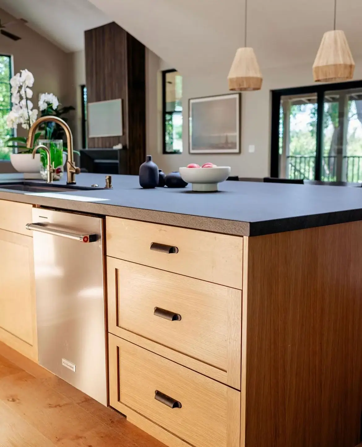 Modern kitchen island with black granite countertop, light wood cabinets, and brass faucet.