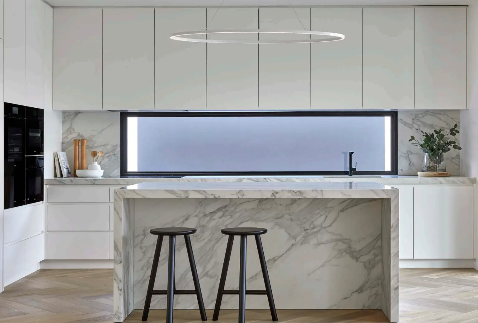 Modern kitchen with white cabinets, Calacatta Royal marble waterfall island, black stools, and linear pendant light