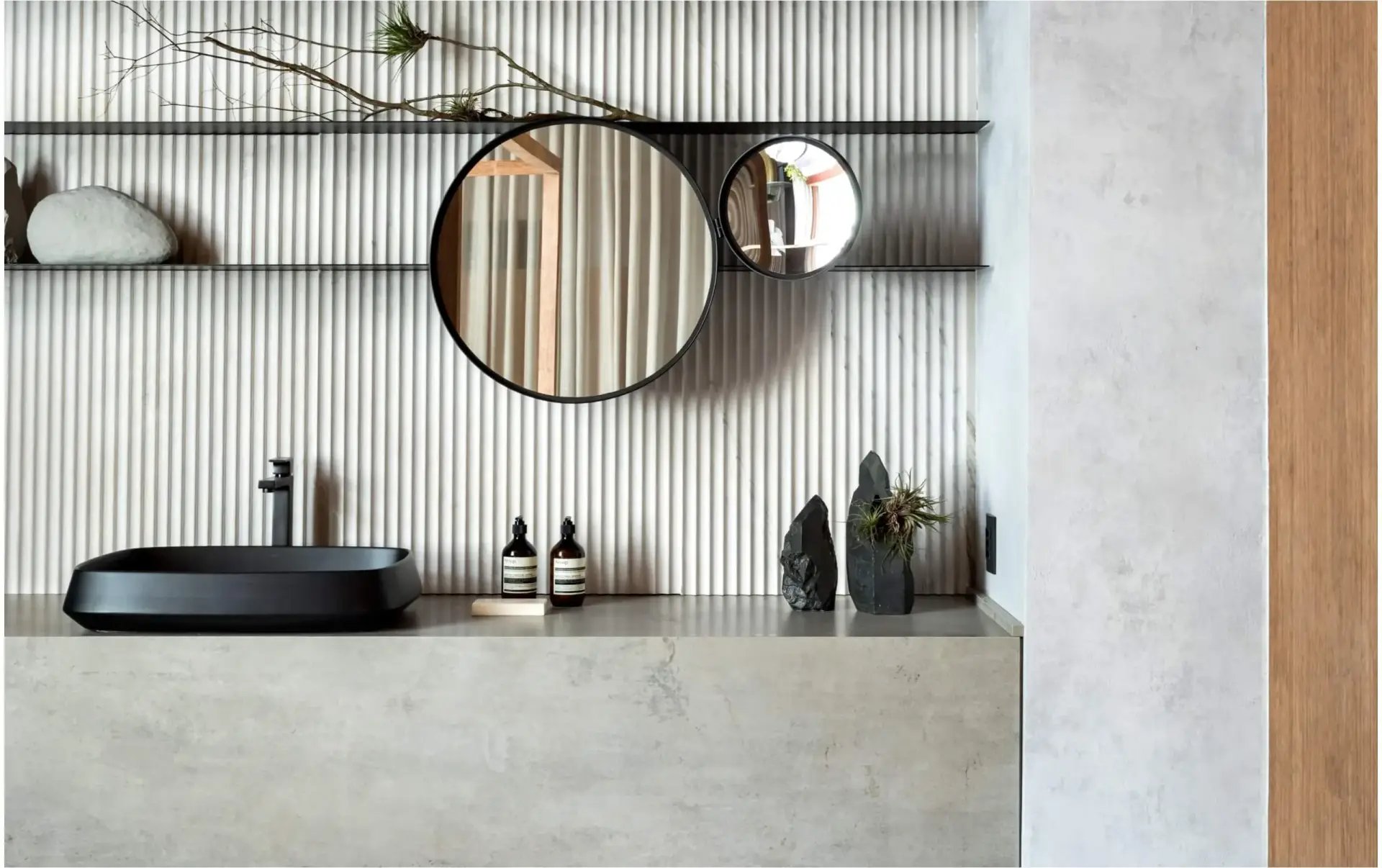 Modern bathroom with black sink, Neolith porcelain countertop, reeded wall tiles, round mirrors, and natural accents.