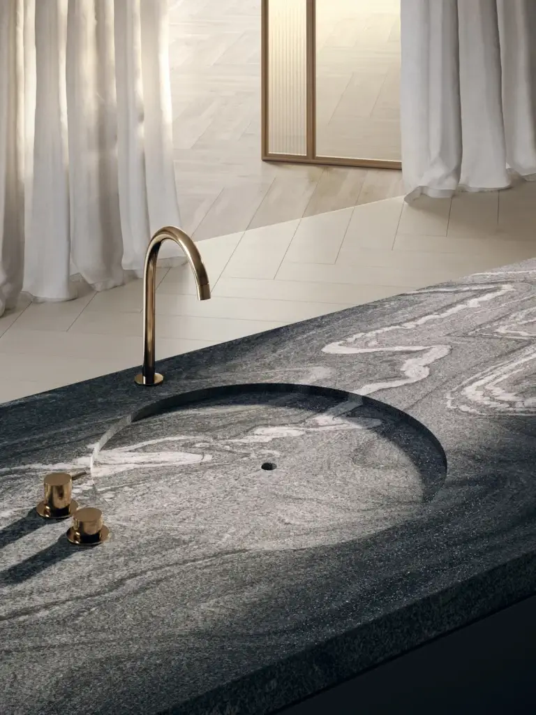 Modern bathroom vanity with dark granite countertop and integrated sink, featuring a gold curved faucet and white curtains.