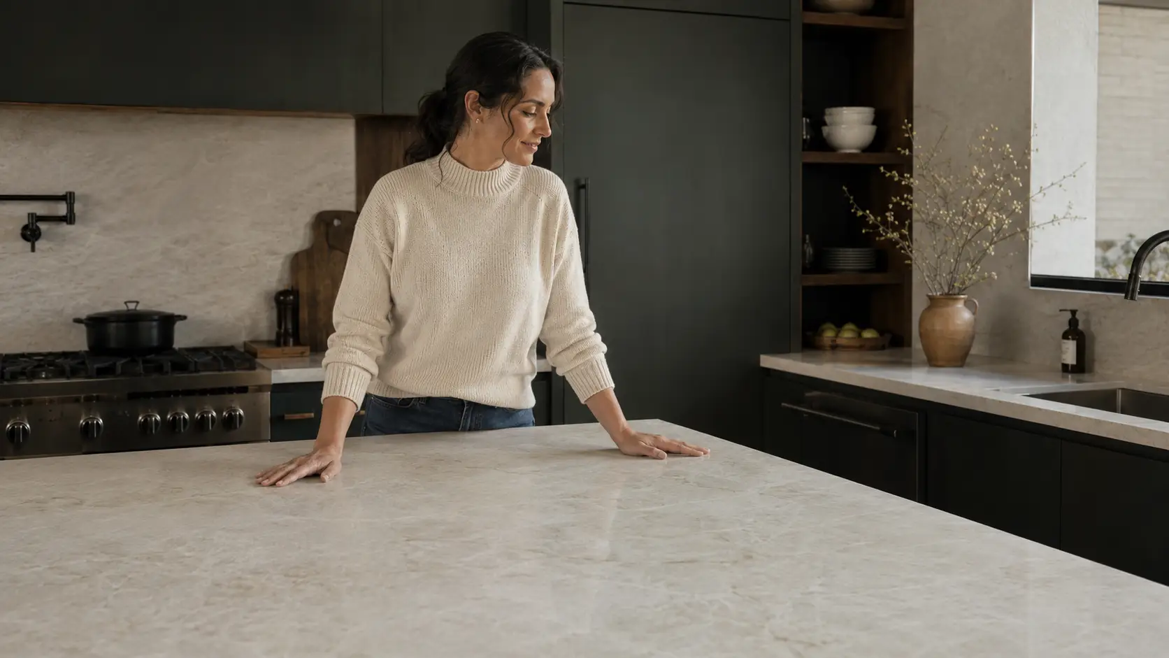 Woman resting her hands on a Honed Taj Mahal quartzite island in a sophisticated dark kitchen