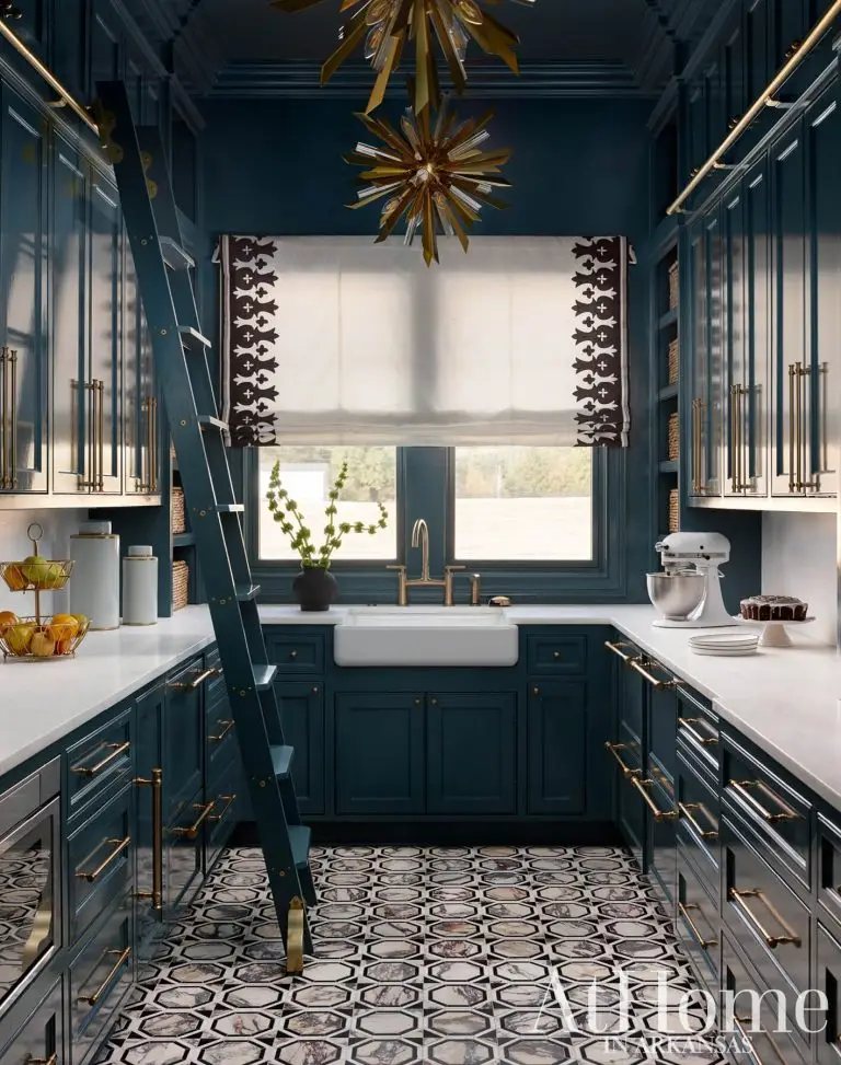 A classic pantry or scullery room with deep teal custom cabinetry and brass hardware. A teal rolling library ladder provides access to upper cabinets.