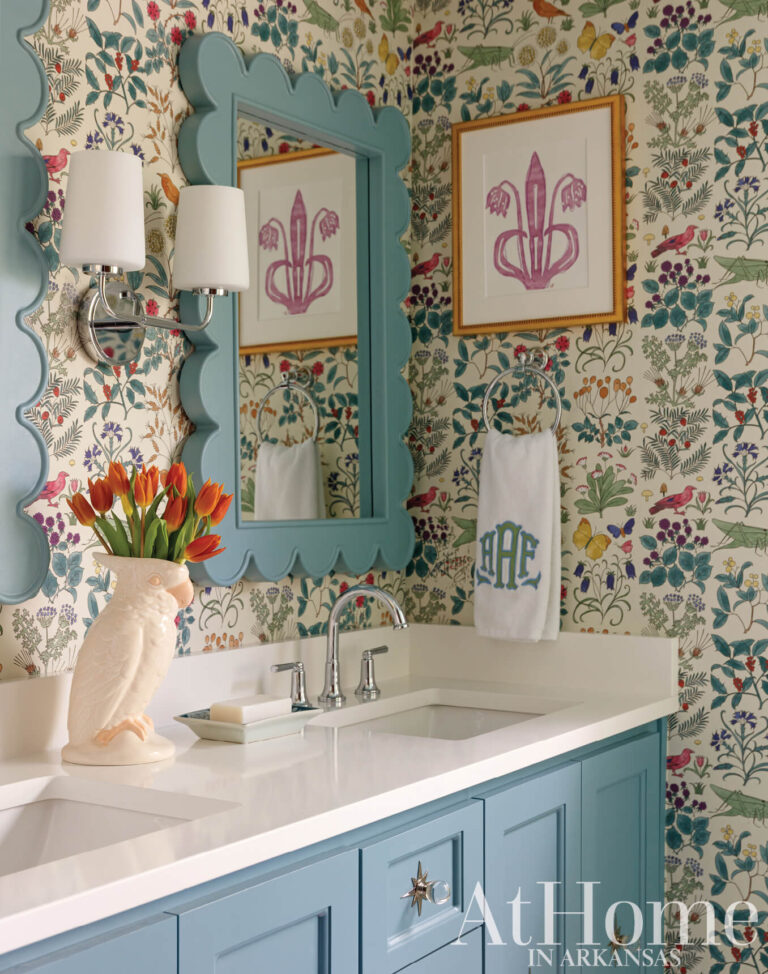 Bathroom with botanical wallpaper, a blue vanity with a white countertop, a scalloped blue mirror, and framed pink prints.