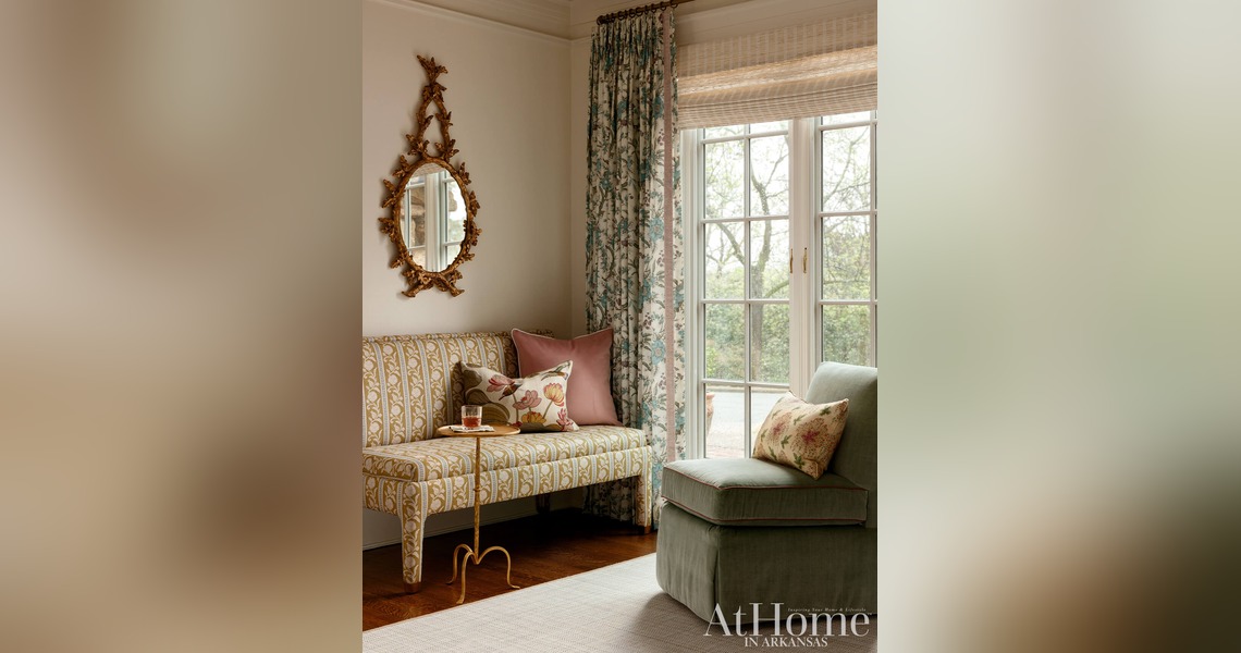 Cozy sitting area with patterned settee, floral curtains, sage green chair and ornate gold mirror