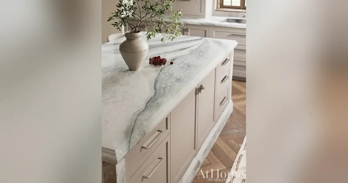 Kitchen island with a Cambria St. Isley quartz countertop veined in soft gray, taupe, and blue over taupe cabinetry.