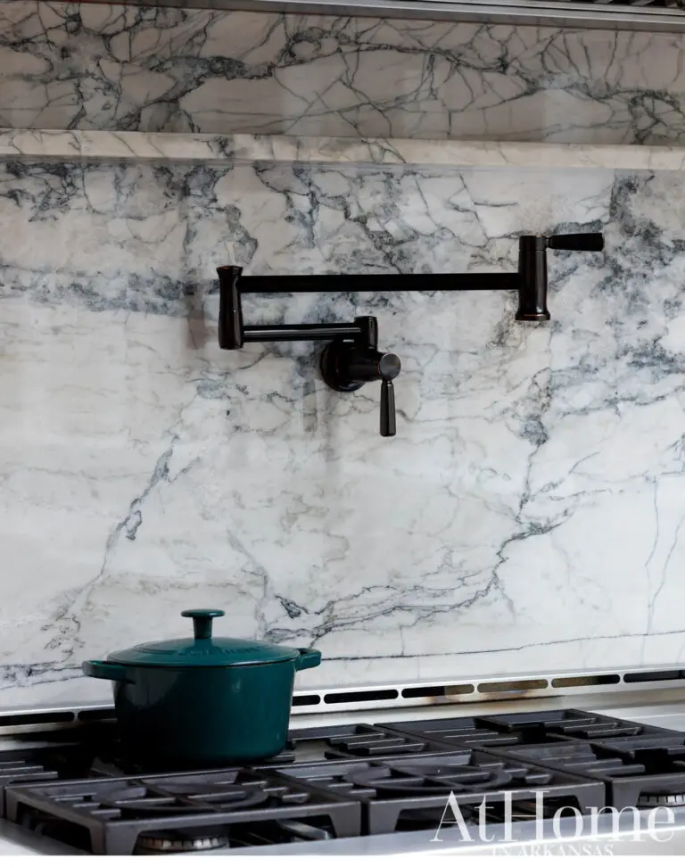 Quartzite slab backsplash with dramatic gray veining behind the range, with a black pot filler and a teal Dutch oven.