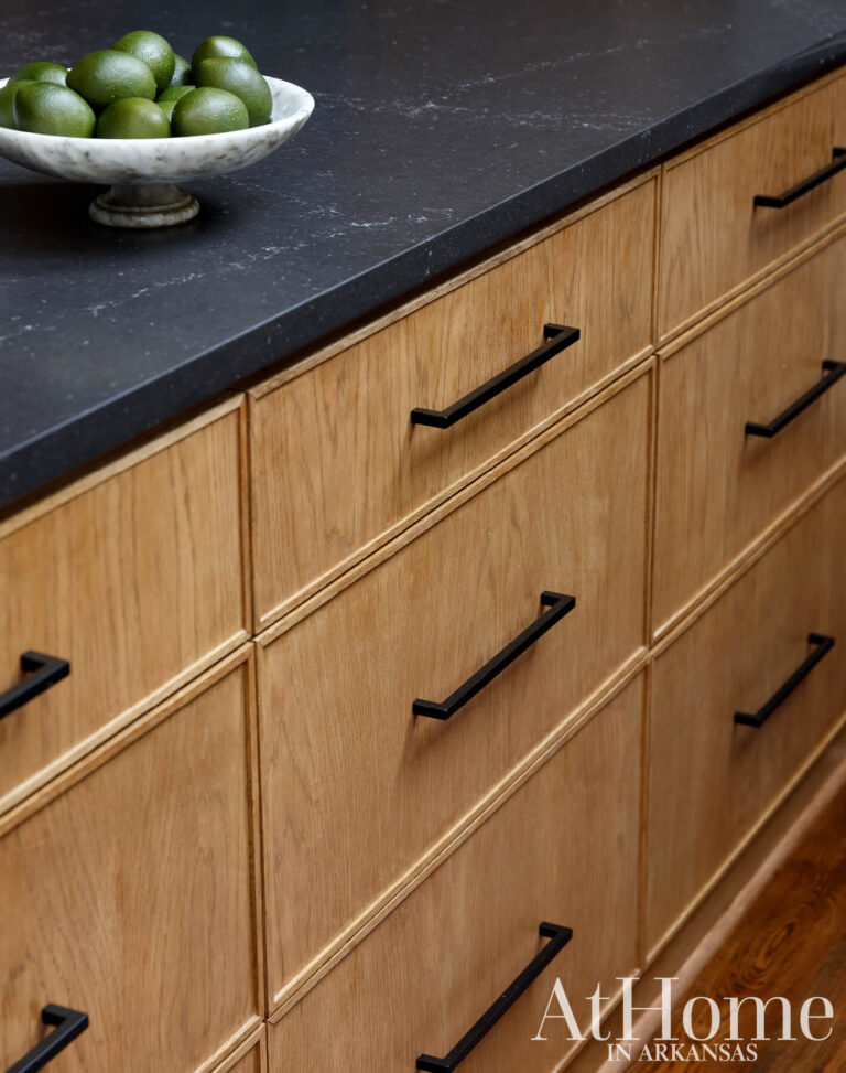 Stained white oak island drawers with black bar pulls beneath a dark countertop and a bowl of limes.