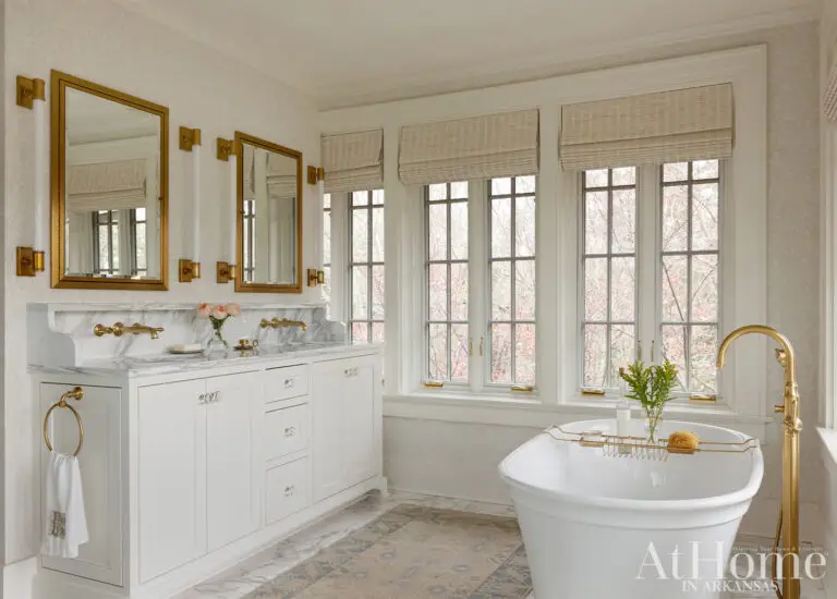 Bright traditional bathroom with a freestanding bathtub, white double vanity, marble surfaces and brass fixtures