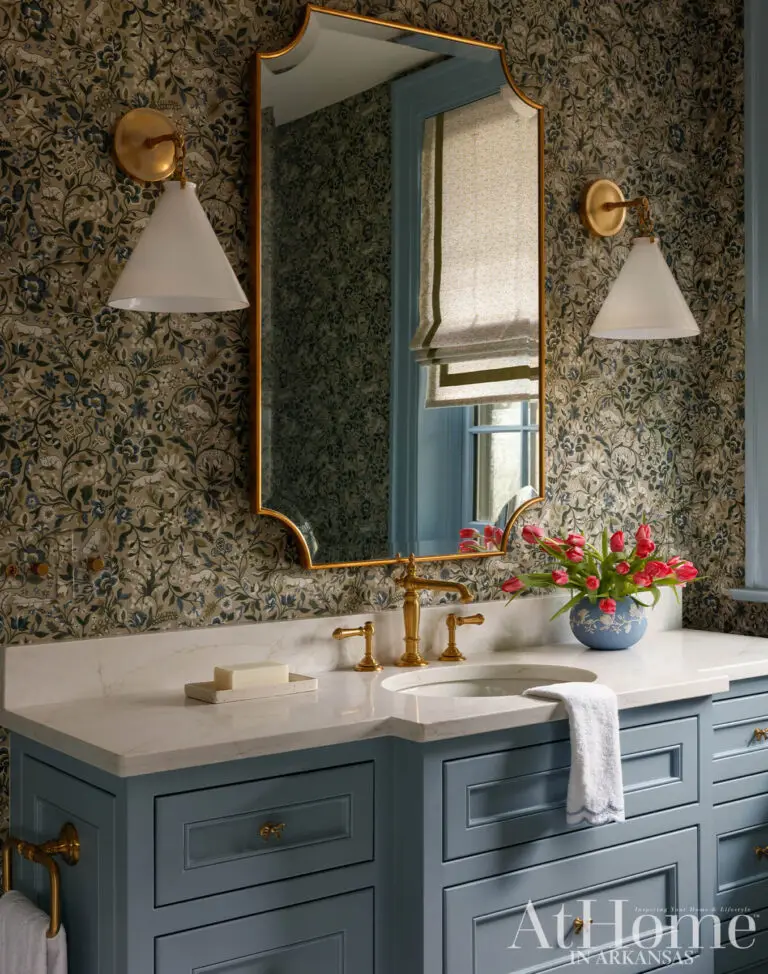 Traditional bathroom with blue vanity cabinets, white stone countertop, floral wallpaper and brass fixtures