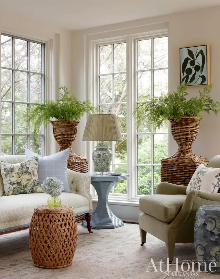 Light-filled sitting room with floral textiles, wicker plant stands and garden views through tall windows
